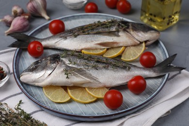 Raw dorado fish with thyme, lemon slices and tomatoes on table, closeup