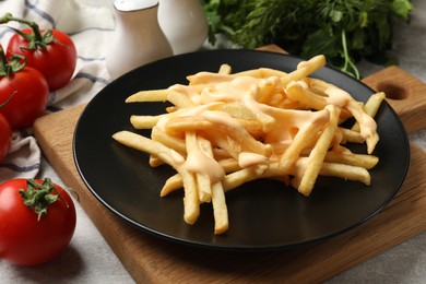 Photo of Delicious French fries with cheese sauce, tomatoes, dill and parsley on grey table, closeup