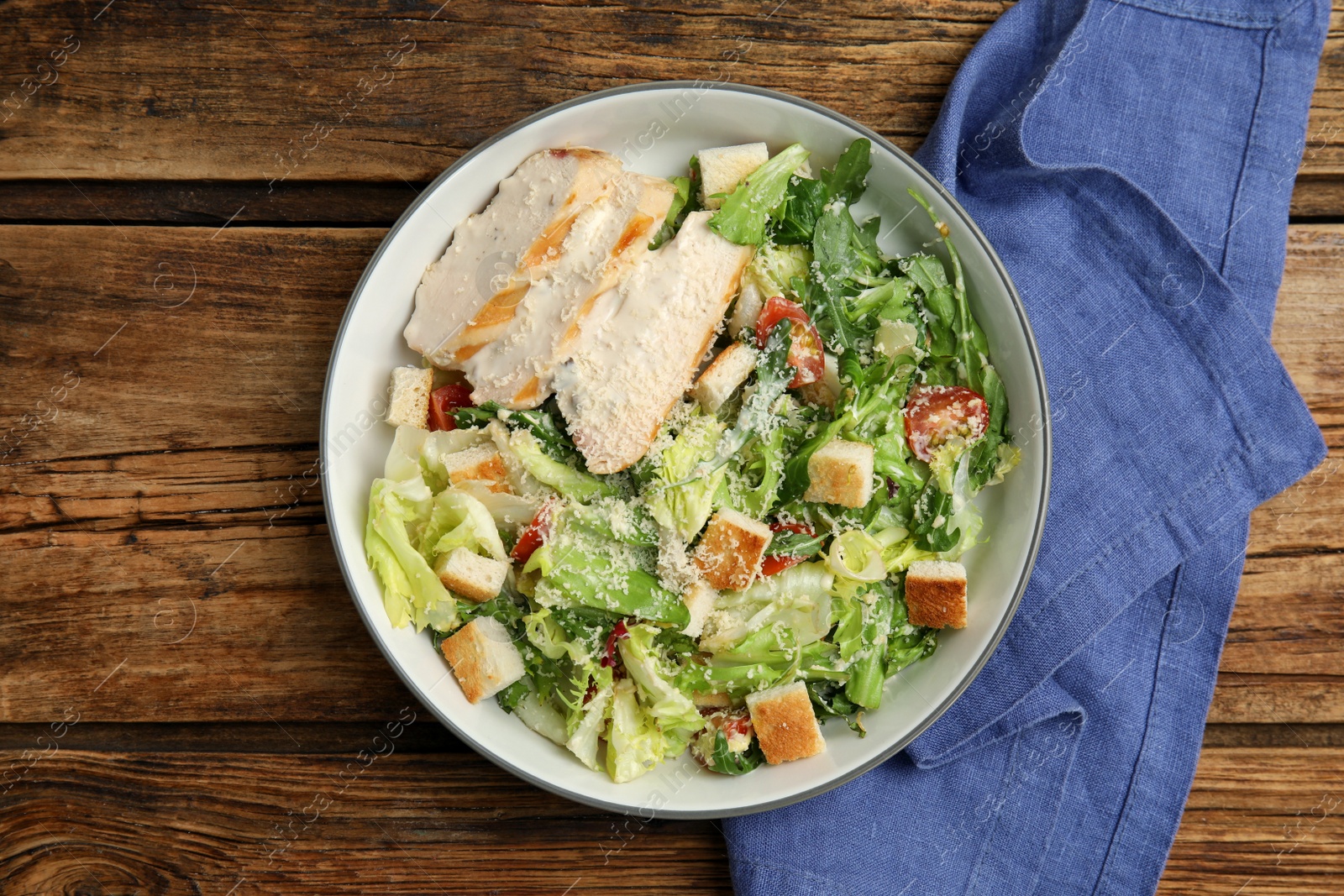 Photo of Delicious Caesar salad in bowl on wooden table, flat lay