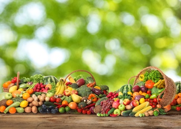 Image of Assortment of fresh organic vegetables and fruits on wooden table against blurred green background