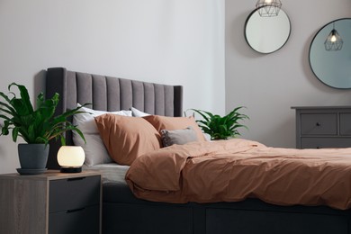 Stylish bedroom interior with comfortable bed and green houseplants