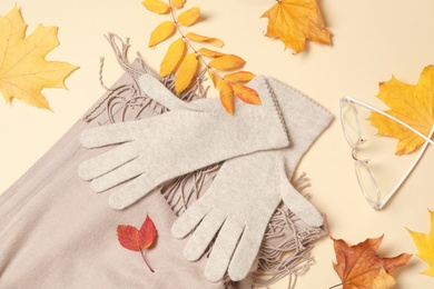 Photo of Stylish woolen gloves, scarf, glasses and dry leaves on beige background, flat lay