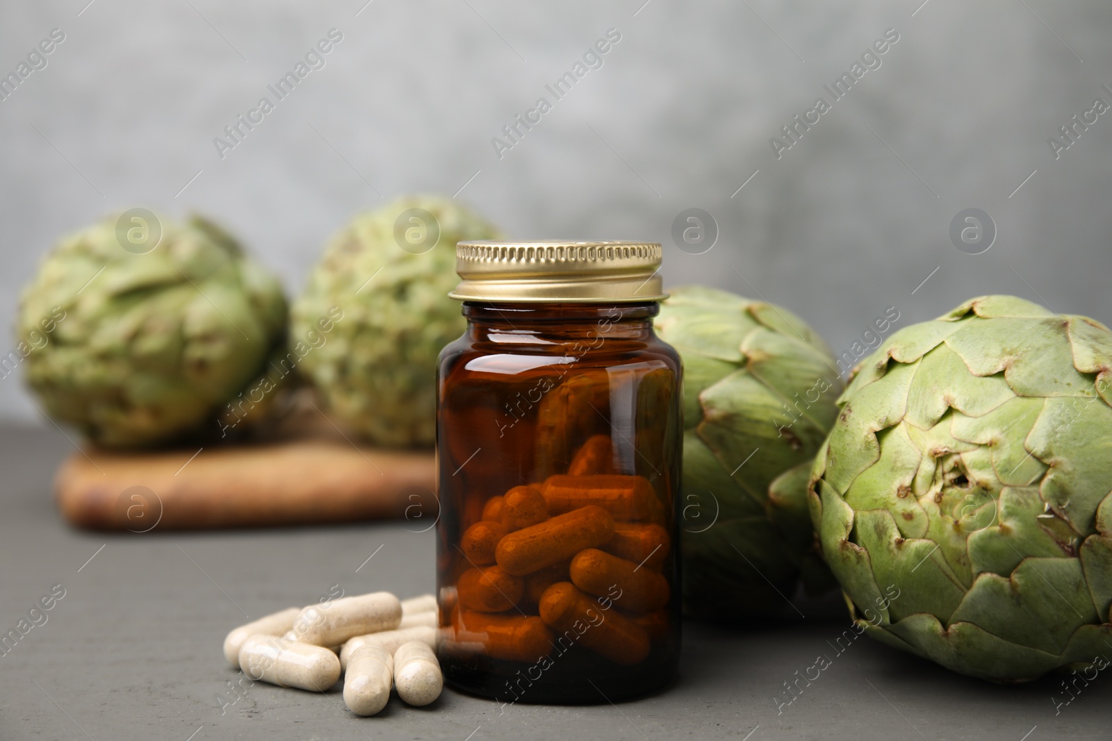 Photo of Bottle with pills and fresh artichokes on grey wooden table, closeup