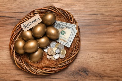 Photo of Golden eggs, money and card with word Retirement in nest on wooden table, top view. Pension concept