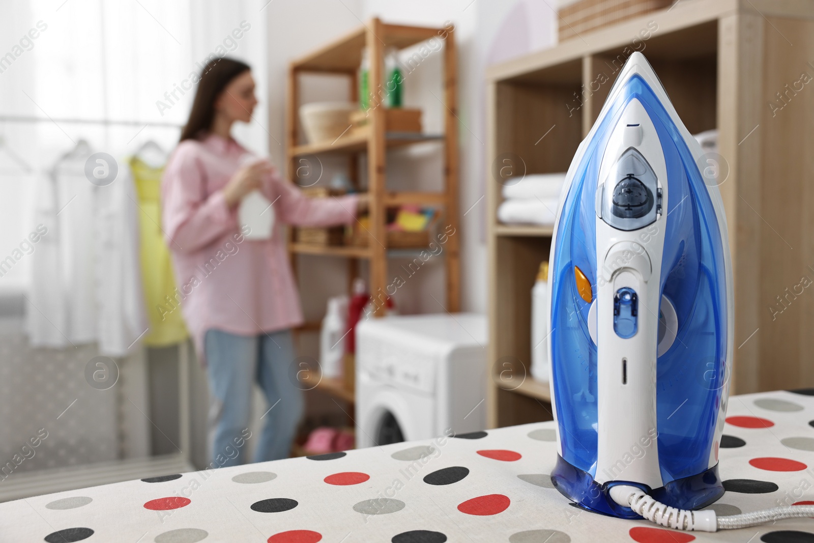 Photo of Woman with detergent, focus on clothes iron in laundry room