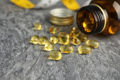 Photo of Bottle with cod liver oil pills and measuring tape on table, closeup