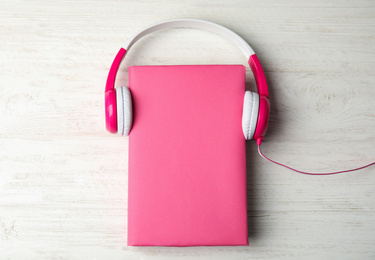 Book with blank cover and headphones on white wooden background, flat lay