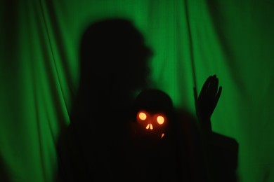 Silhouette of creepy ghost with skull behind dark green cloth