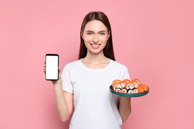 Photo of Happy young woman with plate of sushi rolls and smartphone on pink background. Space for text