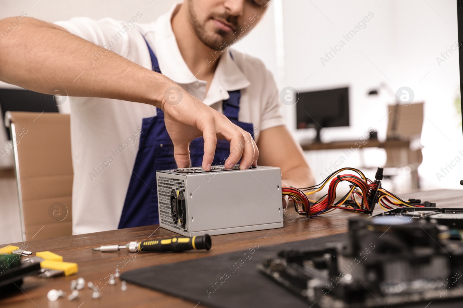 Photo of Male technician repairing power supply unit at table indoors, closeup