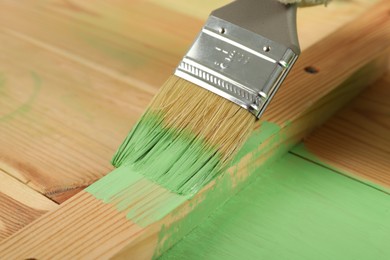Applying green paint onto wooden surface, closeup