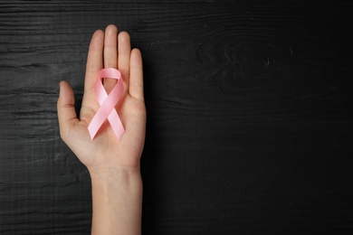 Photo of Young woman holding pink ribbon on wooden background, top view with space for text. Breast cancer concept