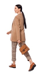 Young businesswoman with stylish bag walking on white background