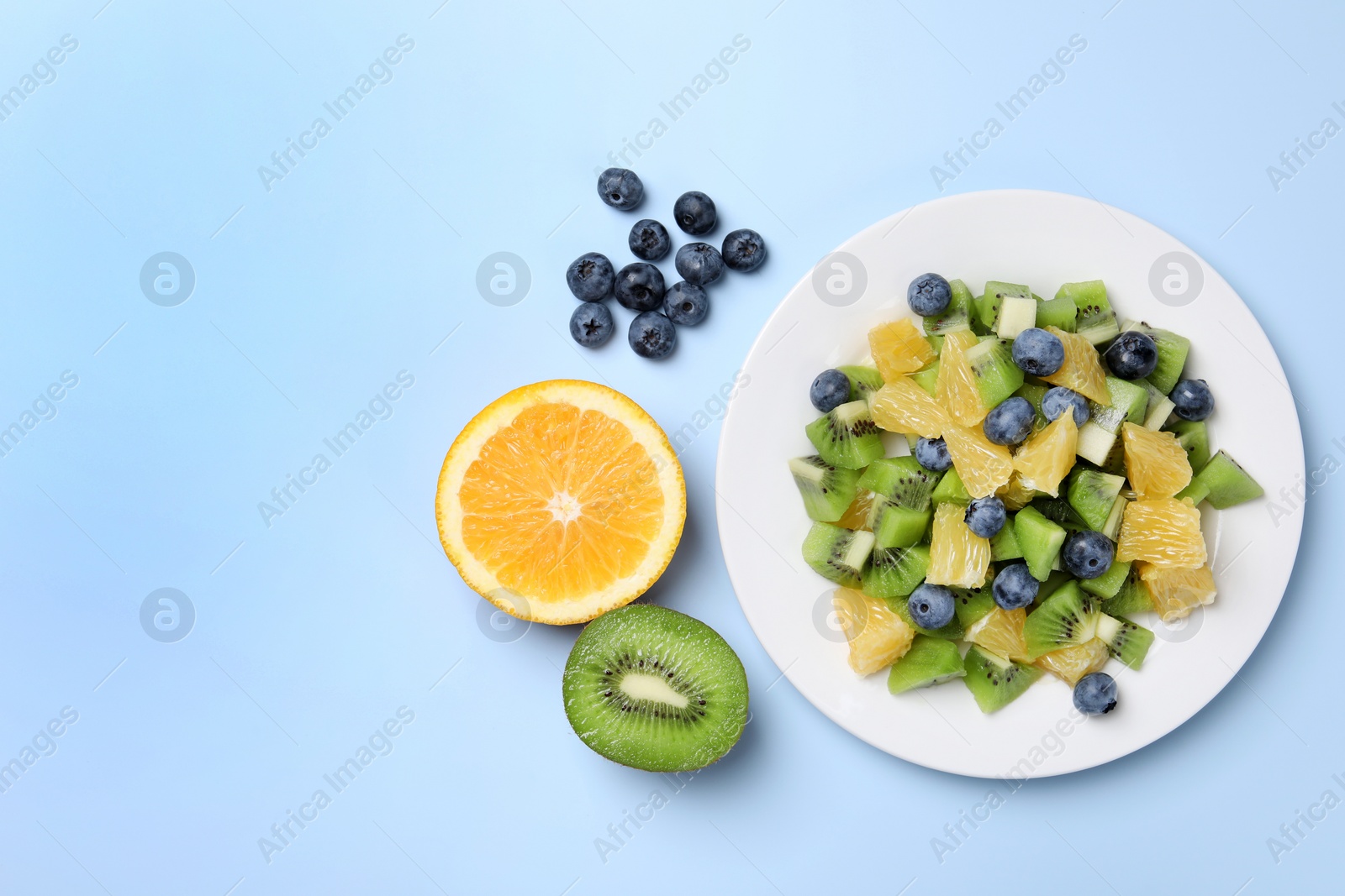 Photo of Plate of tasty fruit salad and ingredients on light blue background, flat lay. Space for text