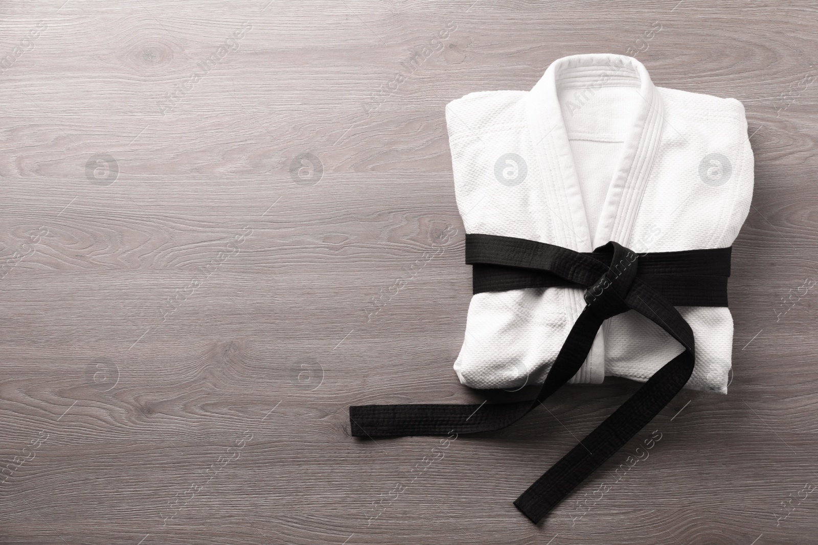 Photo of Martial arts uniform with black belt on white wooden background, top view. Space for text