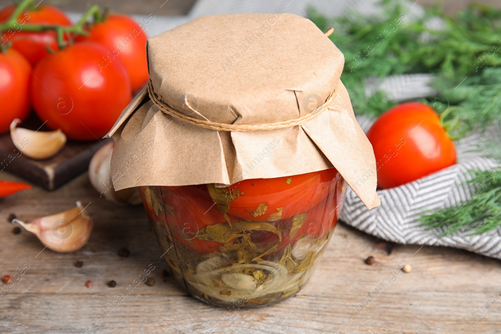 Photo of Pickled tomatoes in glass jar and products on wooden table, closeup