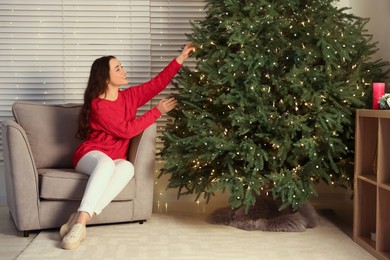 Photo of Beautiful woman near Christmas tree with golden lights in living room