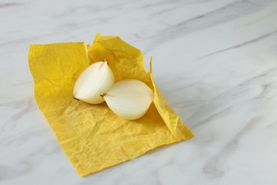 Photo of Halves of onion with yellow beeswax food wrap on white marble table, space for text
