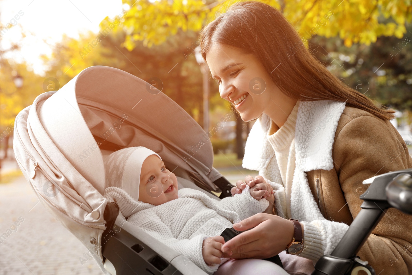 Photo of Happy mother with her baby daughter in stroller outdoors on autumn day