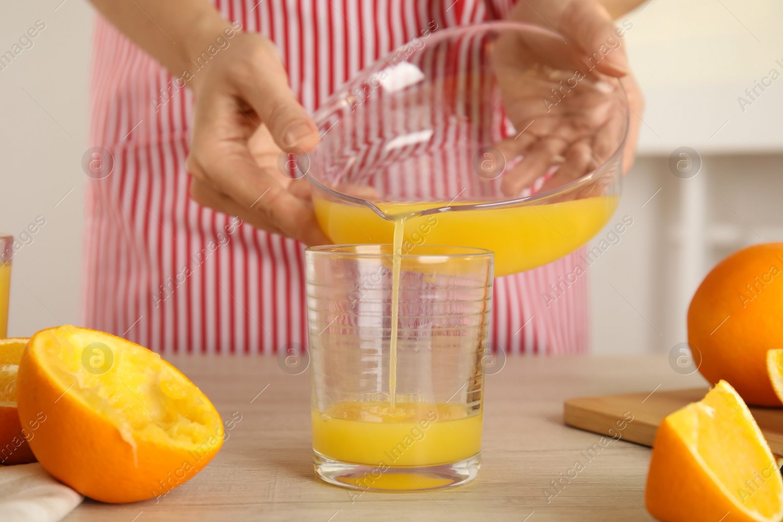 Photo of Woman pouring freshly made orange juice in glass at table, closeup