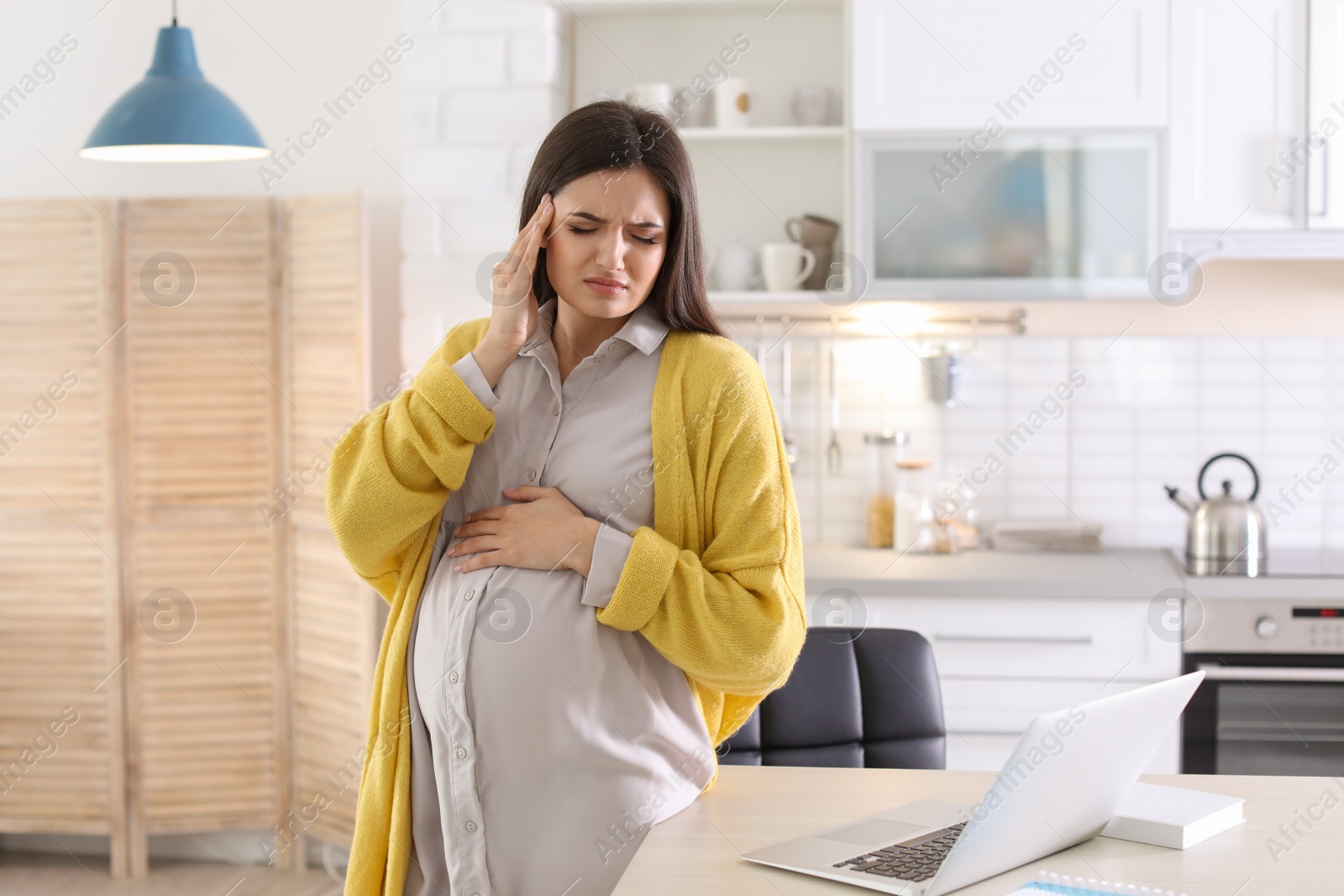 Photo of Young pregnant woman suffering from headache in home office