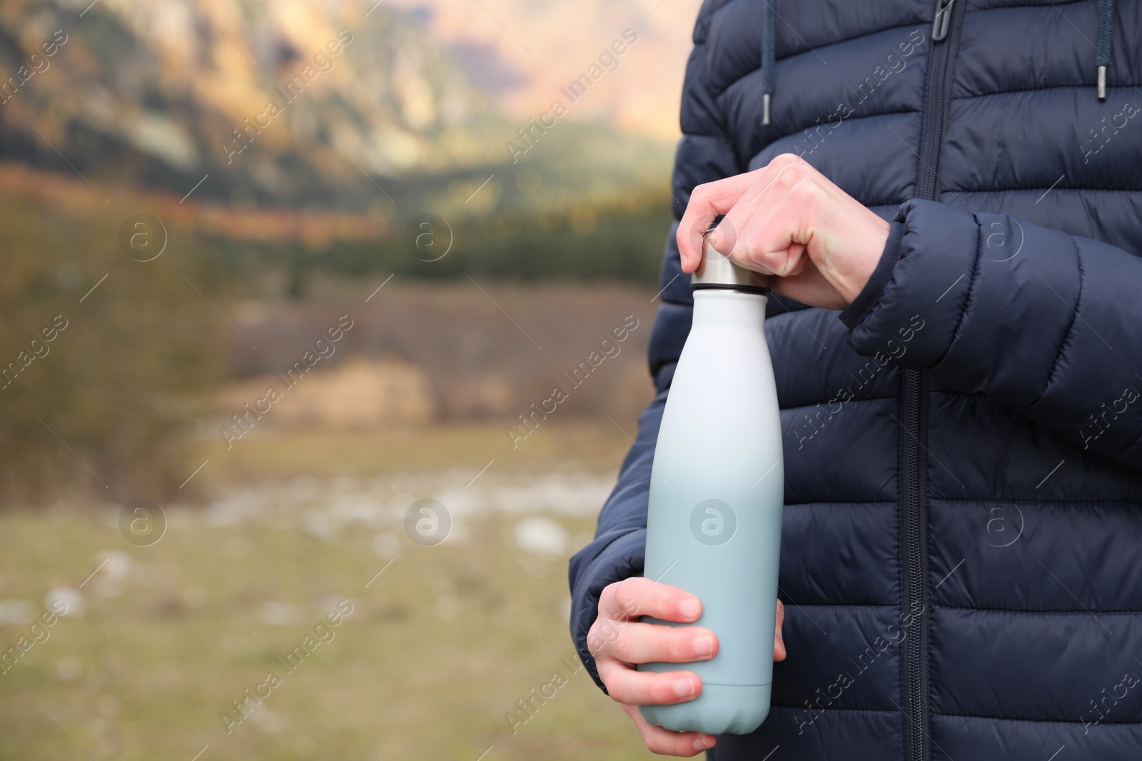 Photo of Boy holding thermo bottle in beautiful mountains, closeup. Space for text