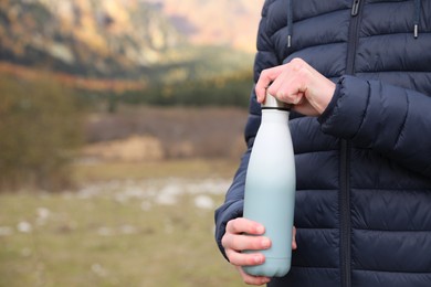 Photo of Boy holding thermo bottle in beautiful mountains, closeup. Space for text