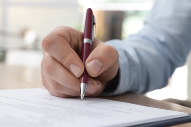 Photo of Man signing contract at table in office, closeup