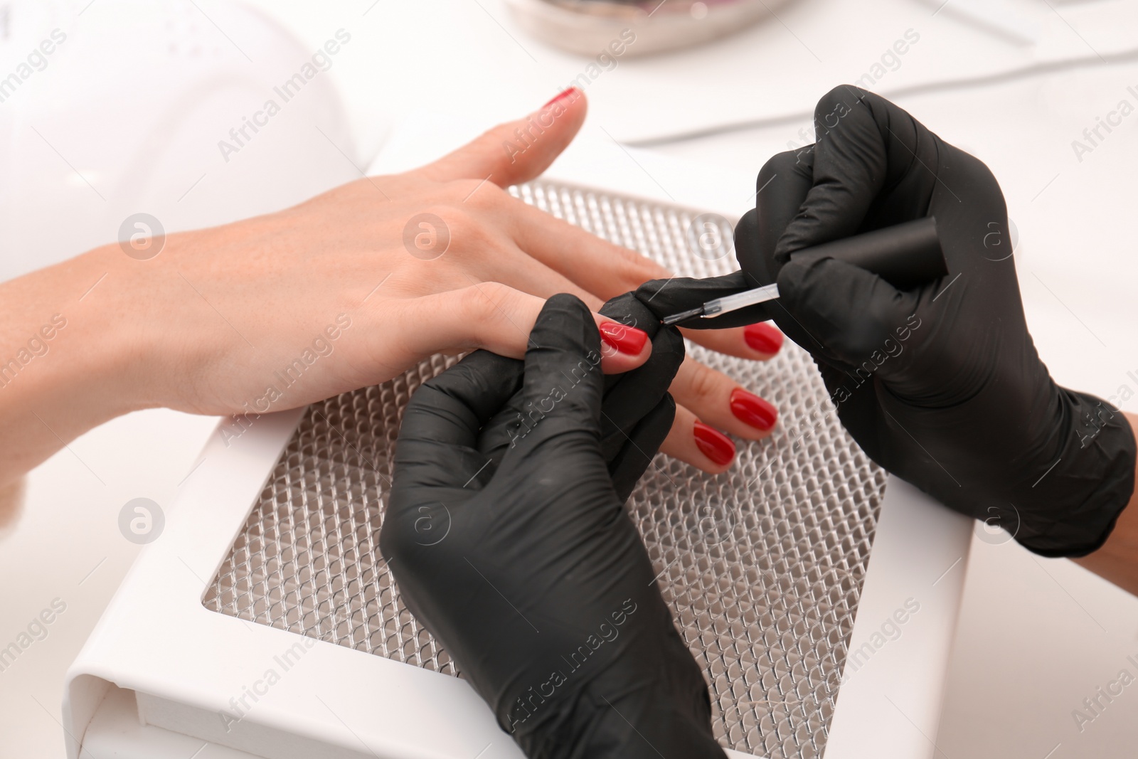 Photo of Professional manicurist working with client at white table, closeup