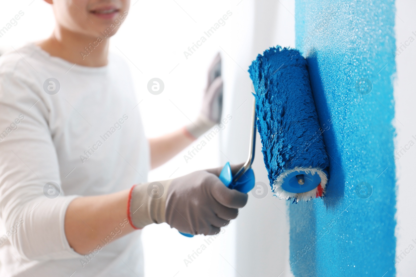 Photo of Male decorator painting wall with roller indoors, closeup