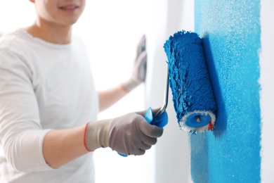 Male decorator painting wall with roller indoors, closeup