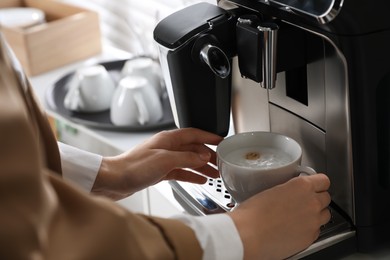 Photo of Woman preparing fresh aromatic coffee with modern machine in office, closeup