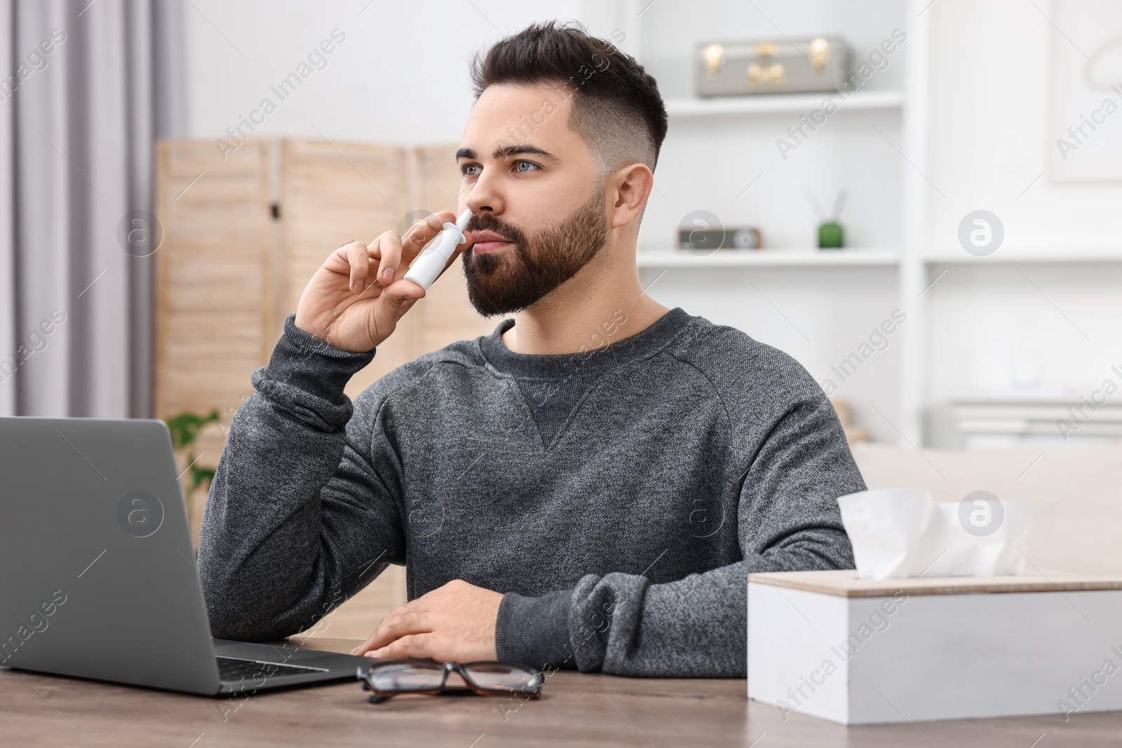 Photo of Medical drops. Young man using nasal spray at table indoors