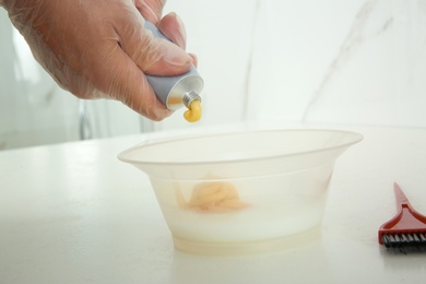 Woman preparing hair dye in bowl at white table, closeup