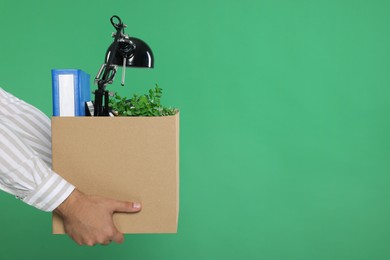Photo of Unemployed man with box of personal office belongings on green background, closeup. Space for text