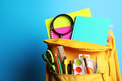 Yellow backpack with different school stationery on blue background, closeup. Space for text