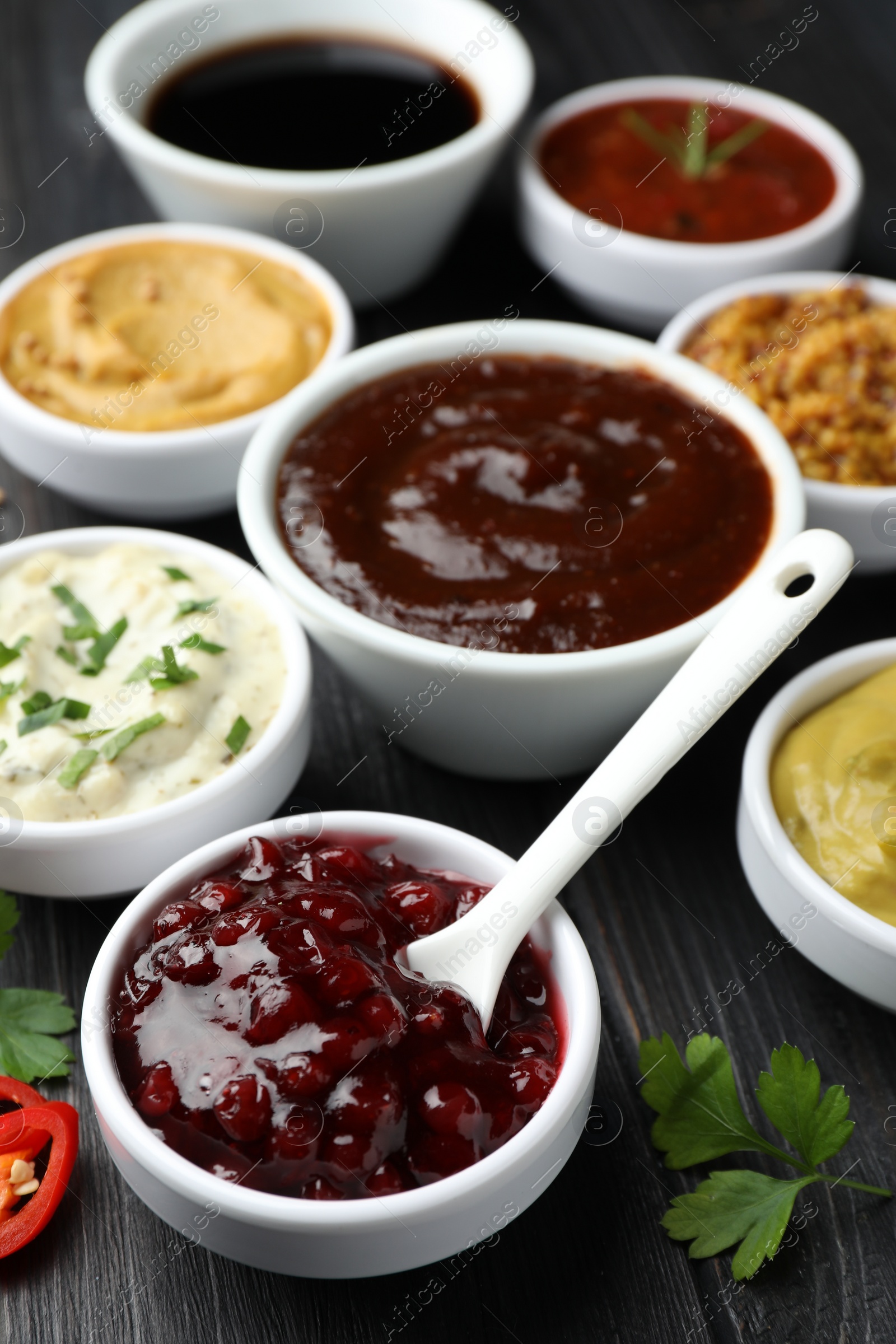 Photo of Different tasty sauces in bowls, parsley and chili pepper on black wooden table