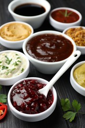 Photo of Different tasty sauces in bowls, parsley and chili pepper on black wooden table