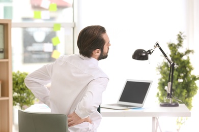 Photo of Young man suffering from back pain in office