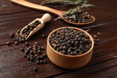 Photo of Aromatic spice. Black pepper in bowl and scoop on wooden table, closeup