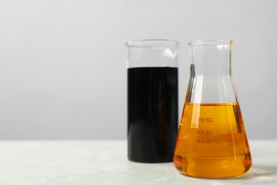 Photo of Beaker and flask with different types of oil on white table, space for text