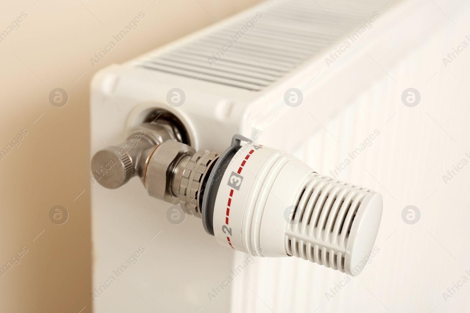 Photo of Heating radiator with thermostat near light wall indoors