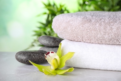 Exotic flower, spa stones and towels on grey table against blurred green background, space for text