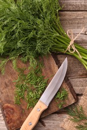 Photo of Fresh dill, cutting board and knife on wooden table, flat lay