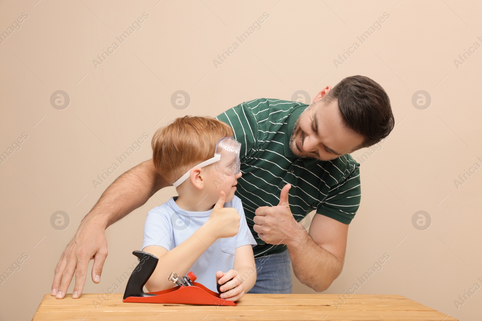 Photo of Father with son showing thumbs up and plane at table near beige wall. Repair work