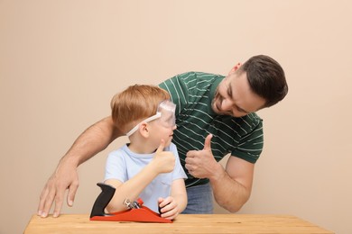Father with son showing thumbs up and plane at table near beige wall. Repair work