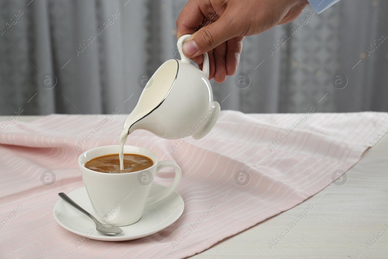 Photo of Woman pouring milk into cup with coffee at table indoors, closeup