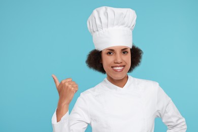Happy female chef in uniform pointing at something on light blue background