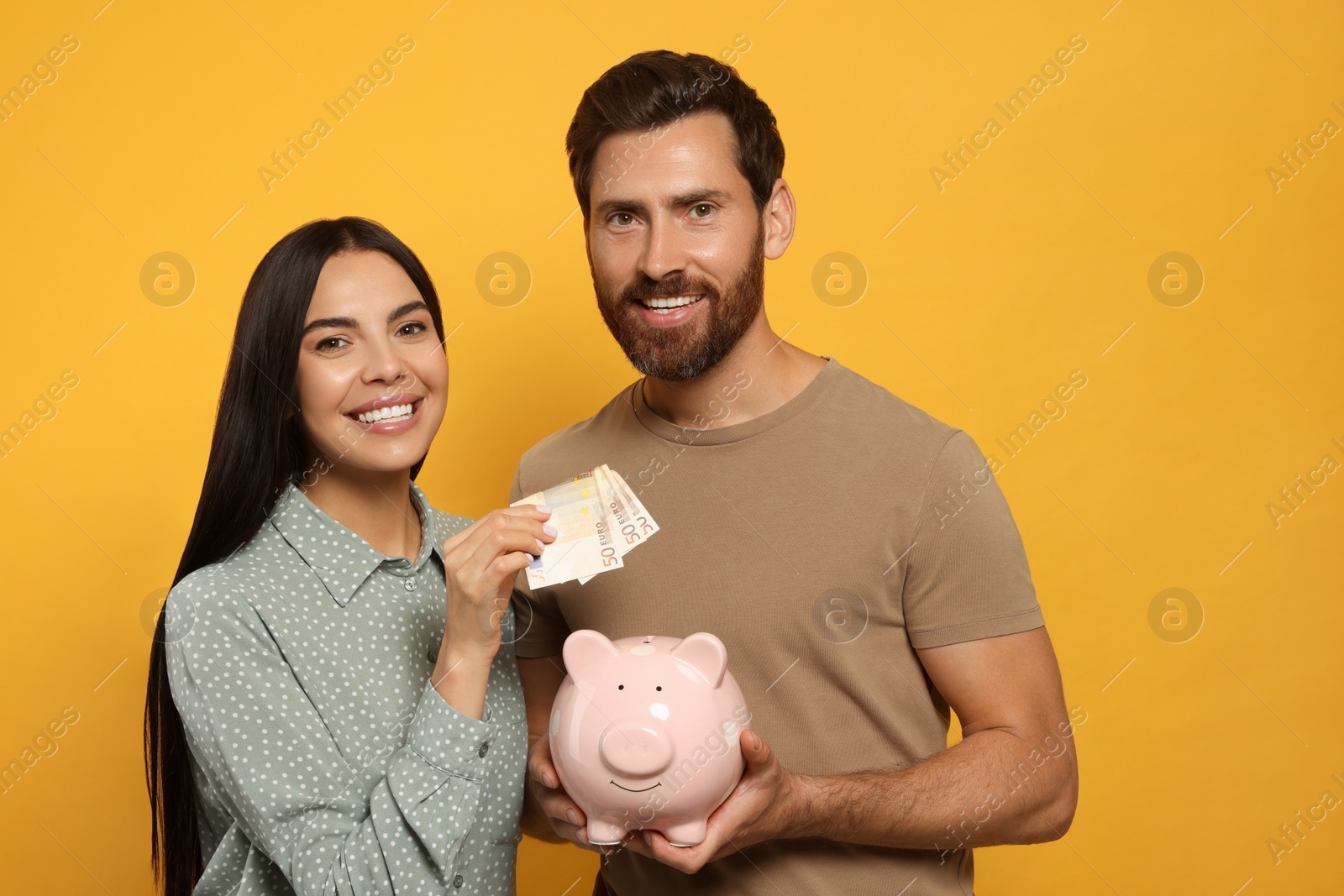 Photo of Happy couple with ceramic piggy bank and money on orange background