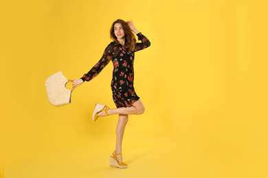 Young woman wearing floral print dress with straw bag on yellow background
